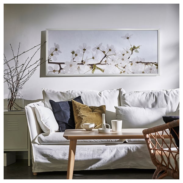 Salon moderne avec art floral au-dessus d’un canapé blanc et d’une table en bois.