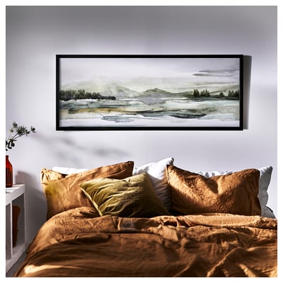 Chambre avec literie aux tons de terre, grand paysage encadré au-dessus, couvre-lit de couleur rouille, oreillers vert olive, petite étagère avec plante et bouteille.