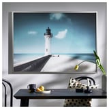 Grand art mural avec phare blanc sur la jetée, ciel bleu. Encadré d’argent, design minimaliste moderne.