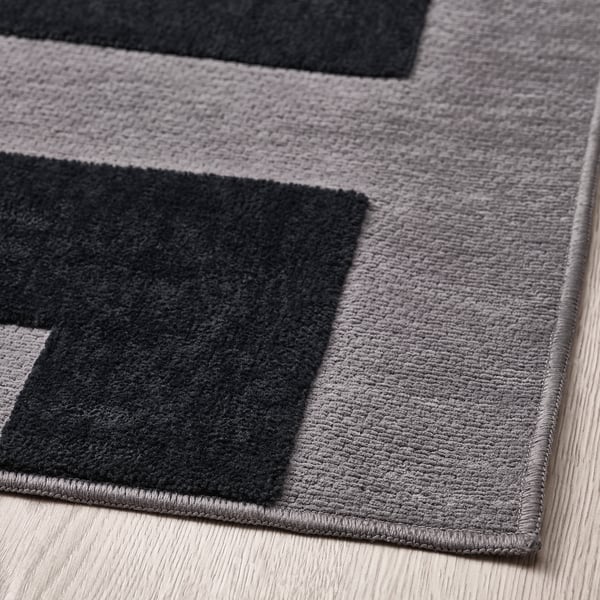 Tapis gris avec des sections noires disposées dans un motif géométrique moderne. Doux, avec une surface texturée, posé sur un plancher de bois franc.