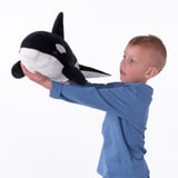 Un garçon en chemise bleue tient une grande baleine en peluche.