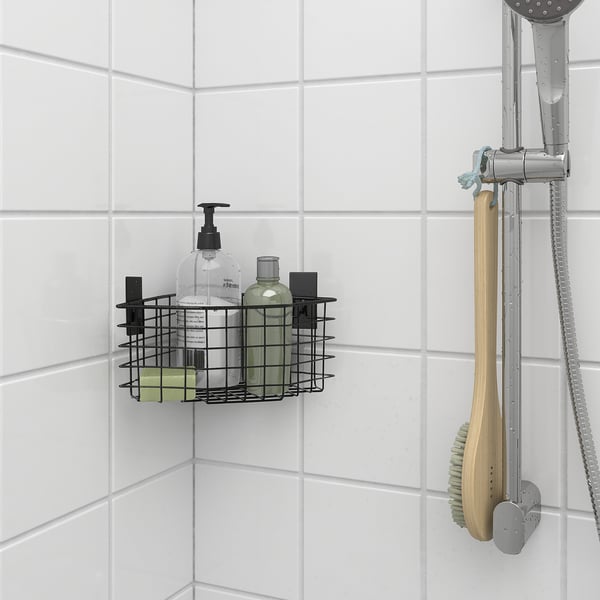 Le panier en fil métallique noir dans la douche contient des bouteilles, monté près de la pomme de douche.