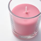 Un gros plan d’une bougie parfumée rose de haute qualité dans un verre transparent, avec une mèche blanche, sur un fond blanc.