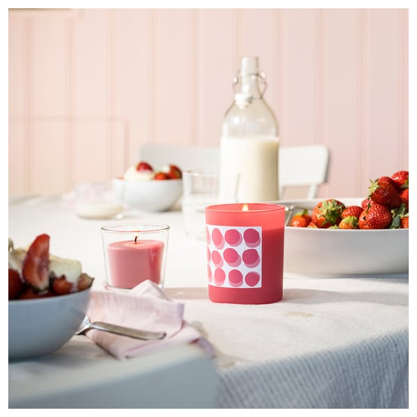 Une table à manger confortable avec une bougie rouge parfumée à la fraise BLODBOK et des bols de fraises.