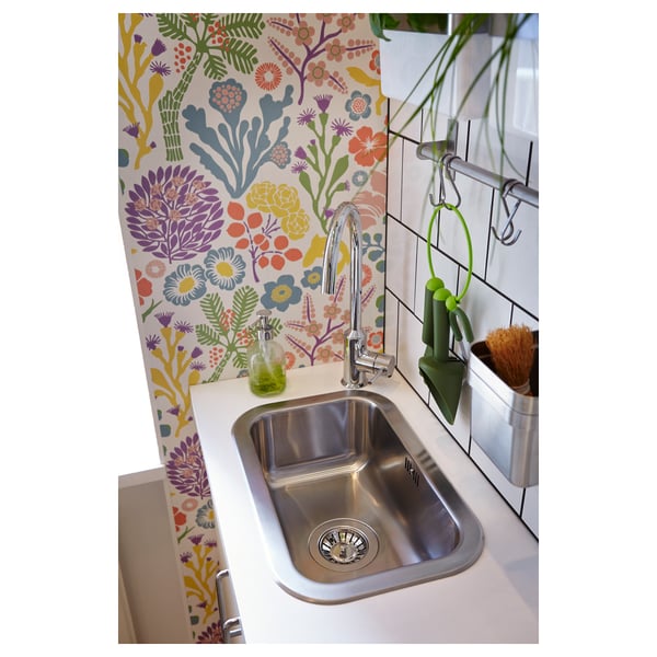 Cuisine lumineuse avec papier peint floral, dotée d’un évier en acier inoxydable, d’un robinet chromé et d’un distributeur de savon vert.