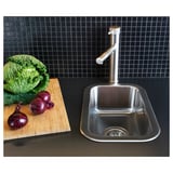 Évier de cuisine moderne en acier inoxydable, design élégant avec robinet, légumes sur planche à découper, dosseret en carreaux de grille noire.