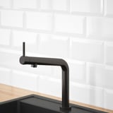 Robinet de cuisine moderne noir avec un indicateur de température rouge, posé sur des carreaux de métro blancs et installé dans un évier noir.