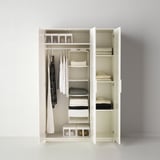 Une armoire blanche avec porte miroir, avec des étagères, des tringles de suspension et des vêtements et accessoires organisés.