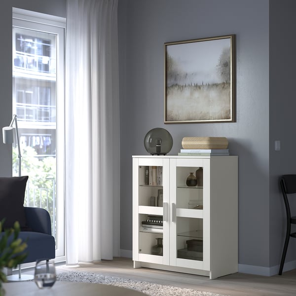 Armoire BRIMNES blanche avec portes en verre, design moderne, s’adapte sous la fenêtre du salon.