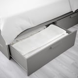 L’image représente un cadre de lit compact avec tiroir coulissant, idéal pour les petits espaces, stockant les draps.