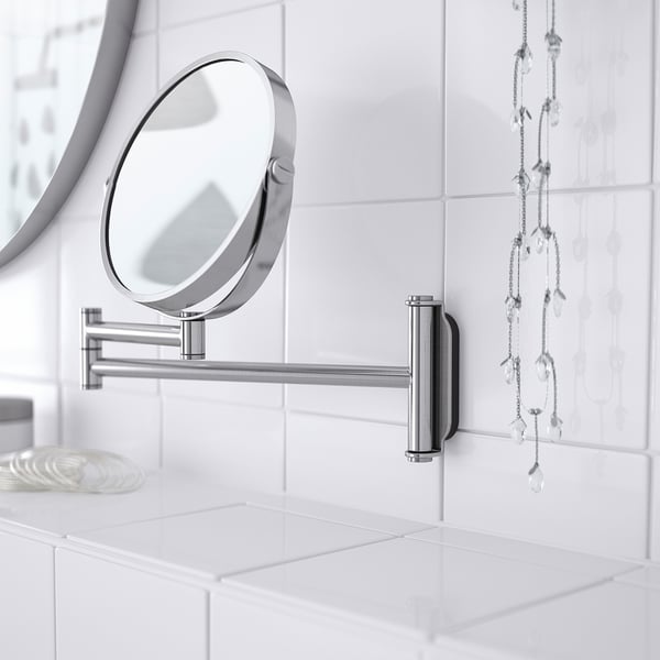 Miroir en acier inoxydable monté avec côté loupe sur le mur carrelé, reflète le cadre propre de la salle de bain.