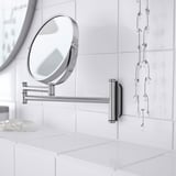 Miroir en acier inoxydable monté avec côté loupe sur le mur carrelé, reflète le cadre propre de la salle de bain.
