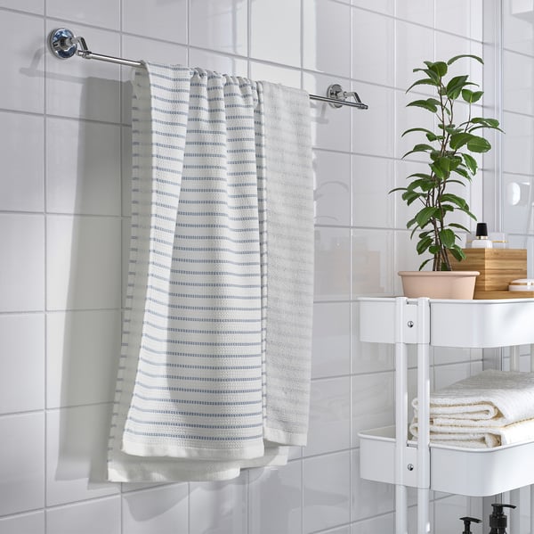 Salle de bain moderne avec une serviette blanche BROKGINST suspendue à un rail à côté d’une petite plante sur un support blanc contenant des serviettes pliées.