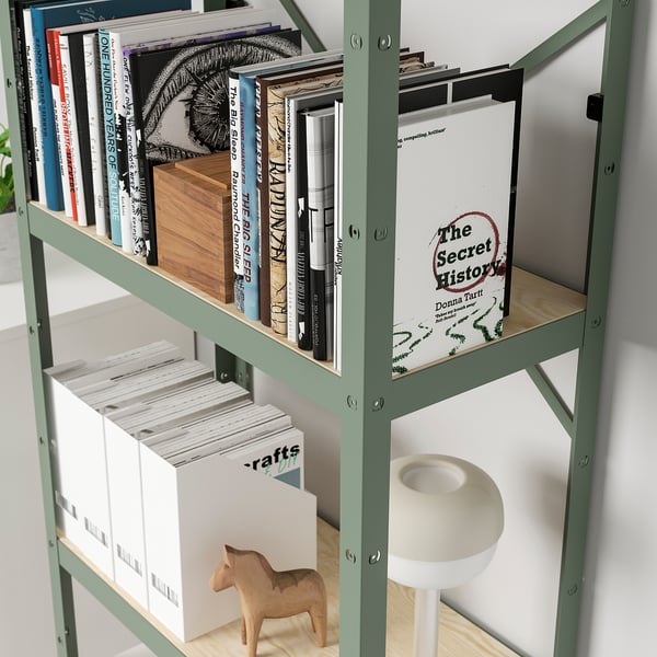 Une étagère en métal vert avec divers objets : des livres, un cheval de bois et des magazines, mettant en valeur ses capacités de rangement robustes et polyvalentes.