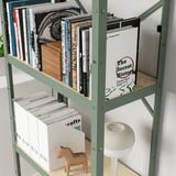 Une étagère en métal vert avec divers objets : des livres, un cheval de bois et des magazines, mettant en valeur ses capacités de rangement robustes et polyvalentes.
