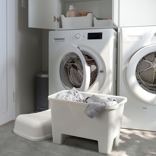 Tabourets en plastique blanc et machines à laver dans la buanderie. Le tabouret central stocke le linge.