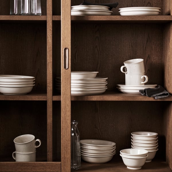 Étagères en bois avec assiettes en grès DAGGASTER beige, bols, tasses, certains enveloppés dans du tissu.