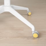 Détail des pieds de la chaise : base en métal blanc solide avec roues jaunes lisses sur plancher en bois clair.