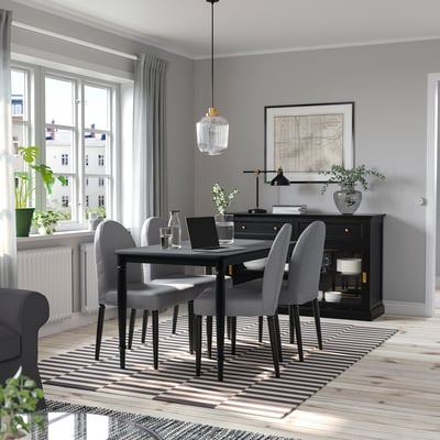 Salle à manger moderne avec table noire DANDERYD et chaises grises. De grandes fenêtres, un tapis rayé et un décor élégant.