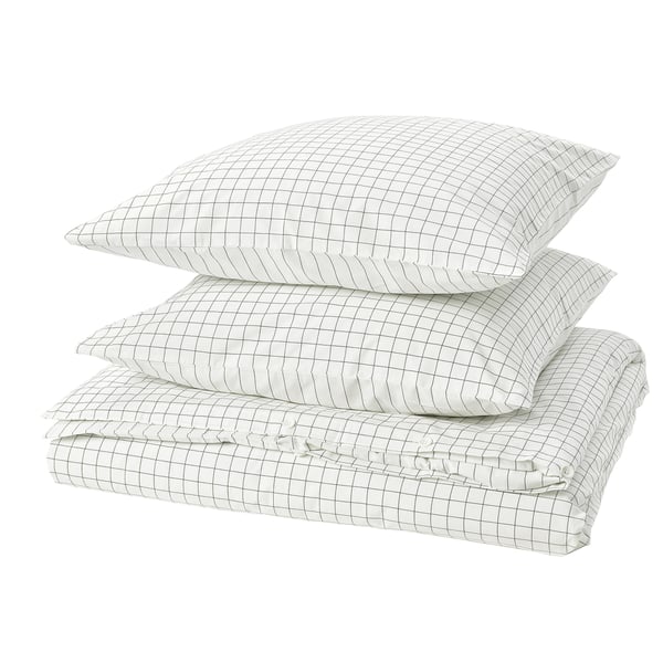 Une pile de linge de lit blanc à motifs quadrillés : couette et oreillers, en coton, soigneusement pliés.