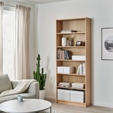 Salon confortable avec des meubles légers. Chaise, tasse, grande étagère, cactus, art mural.