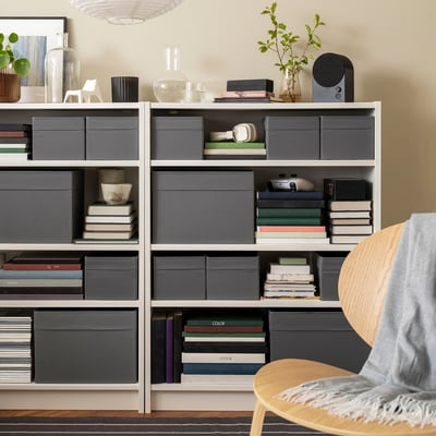 Des boîtes DRÖNA grises sur les étagères, les livres, bols, plantes.