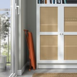 Un support pliant pour ordinateur portable orange était adossé à des armoires blanches aux portes tressées, près d’une fenêtre avec vue sur les arbres.