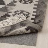 Tapis gris à motifs avec franges sur parquet. Laine tissée à la main, durable, adaptée à divers sols.