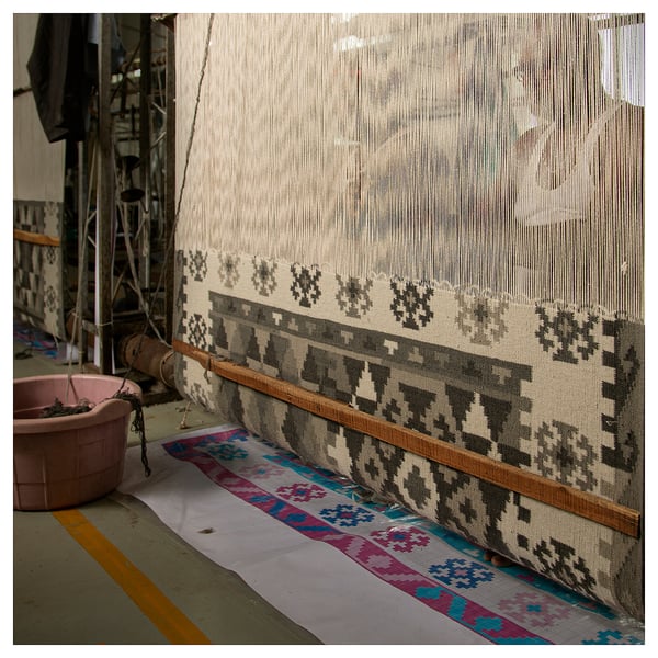 Tapis tissé à la main avec des motifs géométriques gris sur métier à tisser. Mélange de laine et de coton, bords frangés. Fabrication traditionnelle, design moderne.
