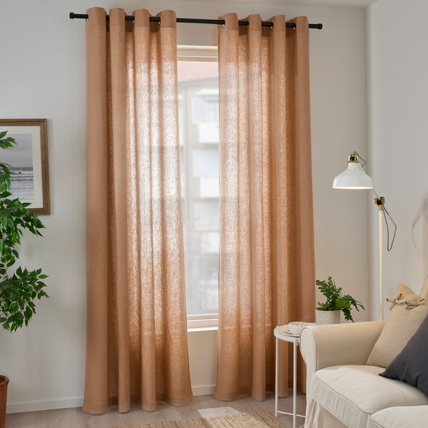 Des rideaux beiges bloquant la lumière sont suspendus dans un salon, flanqués d’une chaise et d’une plante. Le tissu en lin naturel assure l’intimité.