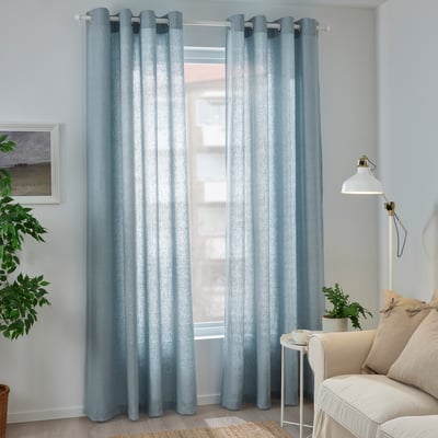 Des rideaux bleu clair pendent près de la fenêtre au-dessus de la chaise beige, offrant de l’intimité et un filtrage doux de la lumière.