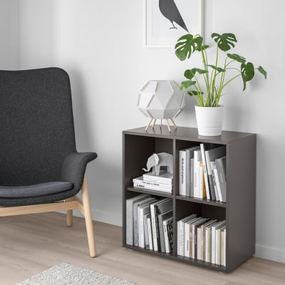 Unité EKET gris foncé avec livres et plantes, à côté d’une chaise grise sur un plancher en bois clair.