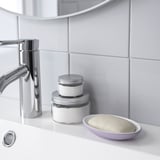 Un robinet chromé brillant à côté de deux pots empilés d’argent et de blanc et un porte-savon à la lavande avec du savon sur un évier blanc.