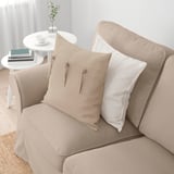 Un canapé EKTORP beige avec des coussins, comprenant un oreiller beige avec des liens et un oreiller blanc, dans une pièce confortable avec une table d’appoint et une décoration.