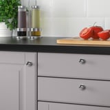 Armoires de cuisine modernes avec des boutons chromés et un comptoir noir, avec une planche à découper avec des tomates et des condiments en tranches.
