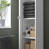 Ouvrez l’armoire blanche montrant des serviettes grises pliées, des bouteilles et des pinceaux.