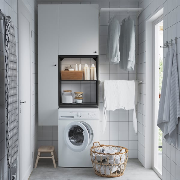 Configuration de blanchisserie blanche moderne avec machine à laver, rangement et espace de penderie. Comprend des étagères avec des fournitures et un panier en osier pour les vêtements.