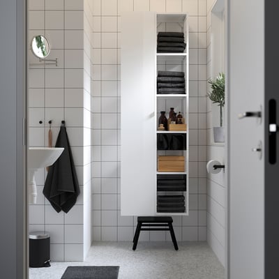 Salle de bain moderne avec armoire haute blanche ENHET et étagères, serviette noire, plante et tabouret. Design élégant et épuré.