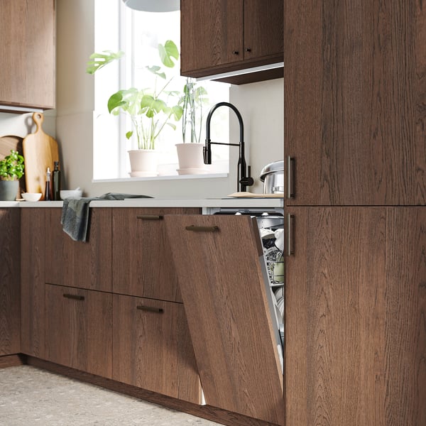 Cuisine moderne avec des armoires en bois sombre, un lave-vaisselle ouvert sous une fenêtre avec des plantes vertes.