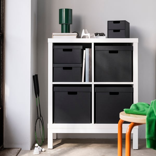 Unité de rangement blanche avec boîtes noires, lampe et vêtements de sport.