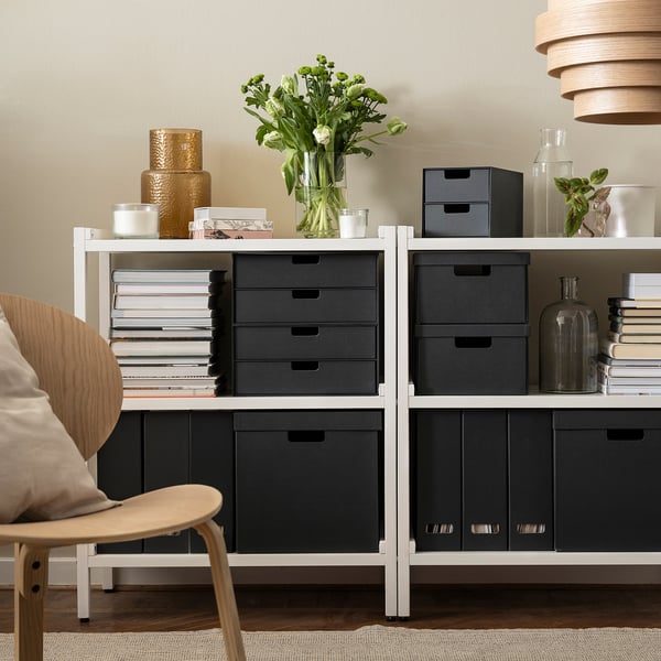Étagère moderne avec FJÄDERHARV boîtes sombres rangeant papiers et livres, vase élégant avec des fleurs, chaises, parquet en bois clair.