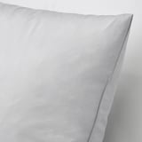 Gros plan d’un coussin doux et garni de duvet avec une housse en coton, mettant en valeur sa texture moelleuse et sa qualité.