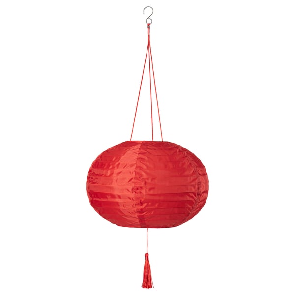 Une lanterne FÖSSTA rouge est suspendue, de forme ovale, de texture soyeuse, avec un pompon, suspendue par des fils rouges.