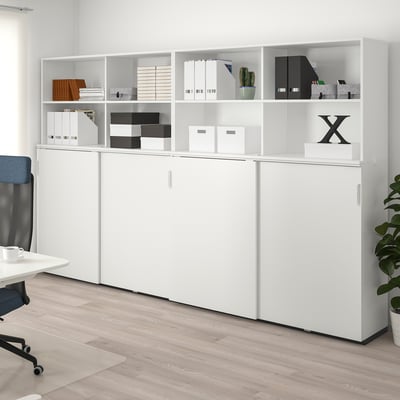 Unité de rangement GALANT avec des sections ouvertes et fermées, organisant les livres, les dossiers et la décoration, à côté d’un bureau et d’une chaise.