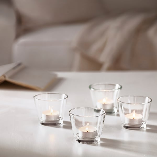 Quatre petites bougies chauffe-plat allumées dans des porte-bougies en verre transparent sur une table, créant une ambiance chaleureuse et confortable.