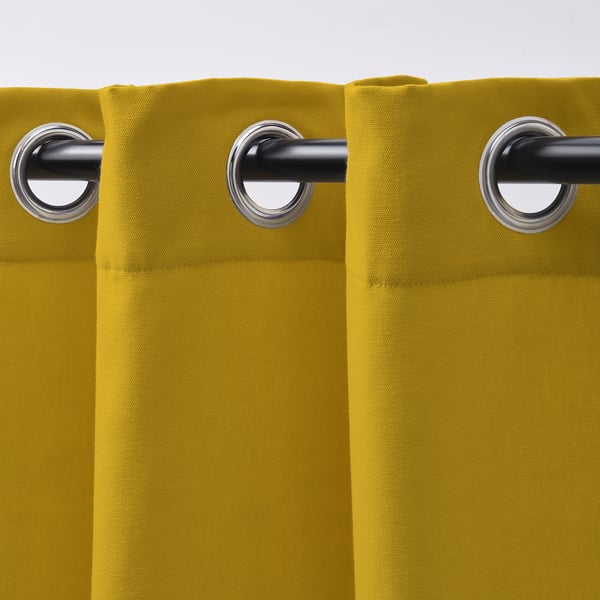 Des rideaux jaune vif avec de grands œillets argentés pendent soigneusement, offrant un style moderne et filtrant la lumière.