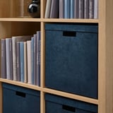 Bibliothèque en bois avec des boîtes de rangement en velours et des livres colorés.