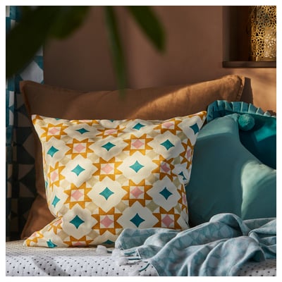 Housse de coussin aux couleurs vives et à motifs multiples sur un lit, avec des motifs géométriques aux teintes vives, en 100 % coton.