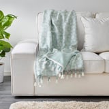 Un plaid bleu clair avec des pompons blancs sur un canapé beige ajoute du confort et un style ludique.