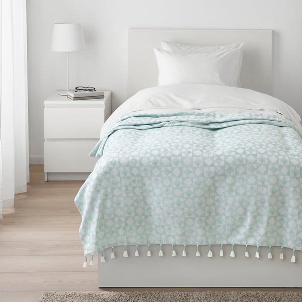 Jeté GOKVÄLLÅ bleu avec motifs géométriques blancs sur le lit.